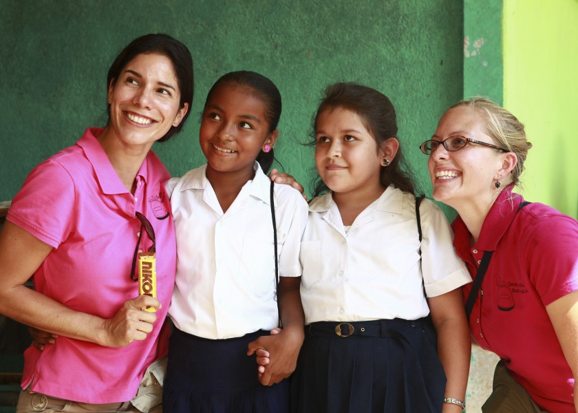 Janina Viteri, left, and Kari Williams, right, with the nongovernmental organization group Give a Kid a Backpack, and two students pose for a photo after giving the children backpacks filled with school supplies 100825-M-PC721-024